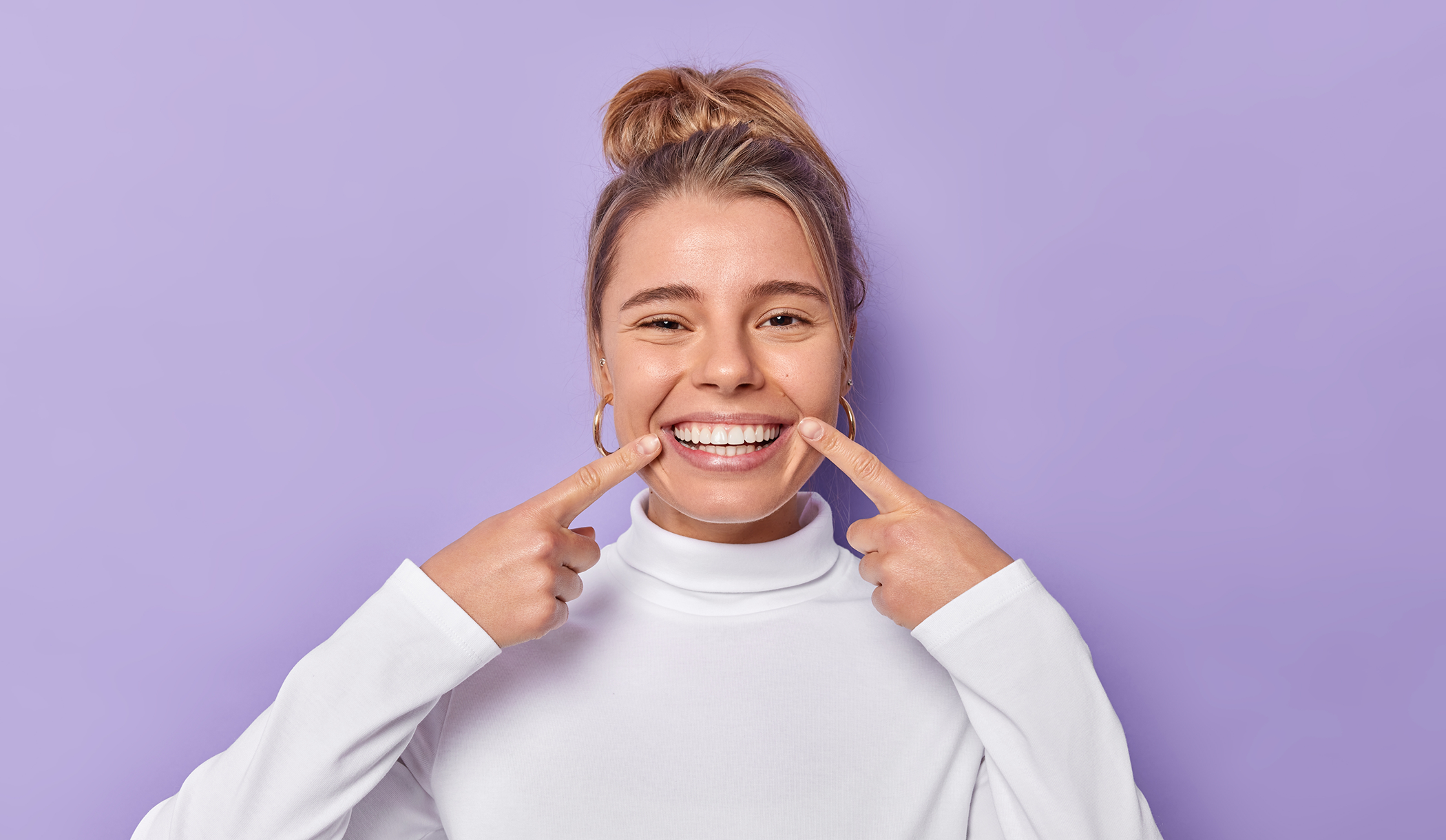 Young woman pointing to her flawless smile after getting veneers in Wakefield