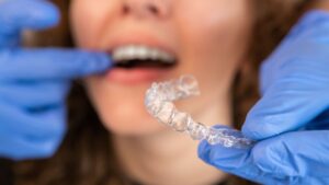 Dentist with blue gloves holding Invisalign in one hand and touching patient's teeth with the other